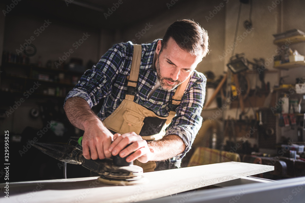 Carpenter at workshop polishes wooden board with a electric orbital sander