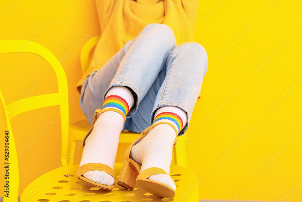 Young woman in socks and sandals sitting on chair against color background