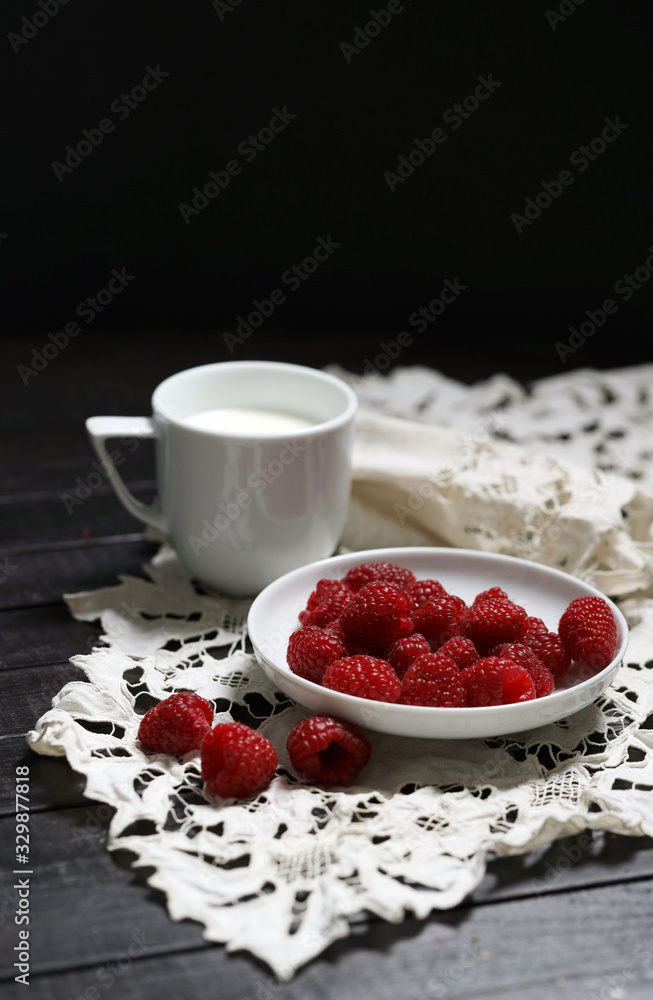 把成熟的树莓放在白色盘子里，把浆果放在一边，把一杯牛奶放在白色手巾上。