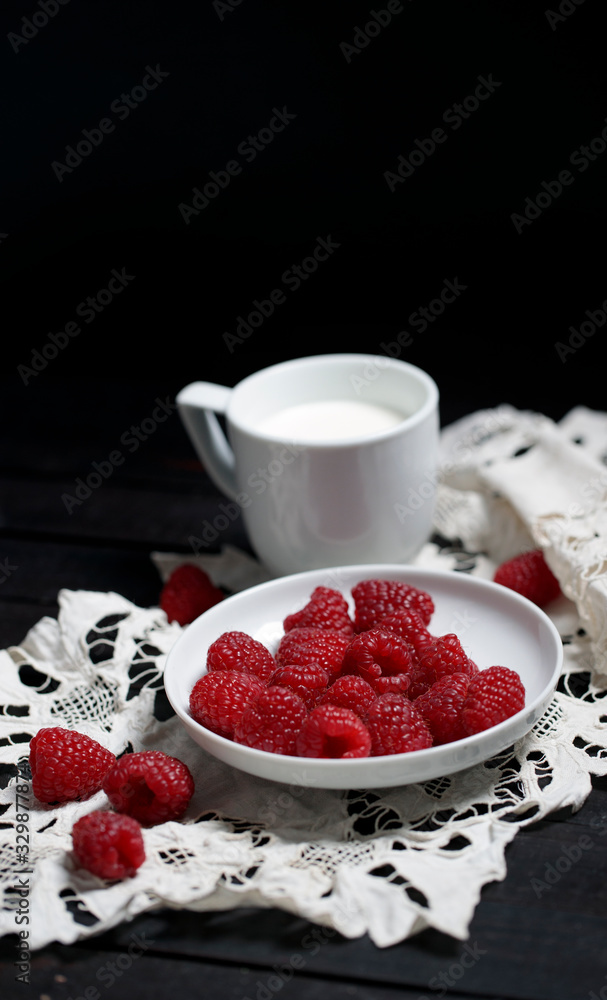 把成熟的树莓放在白色盘子里，五个浆果放在一边，一杯牛奶放在白色手巾上。