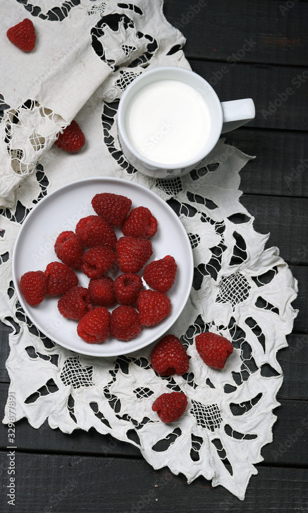 白色盘子里的成熟树莓和浆果的俯视图，旁边放着一杯牛奶，放在白色的手指甲上