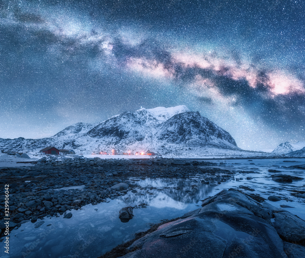 冬季夜晚，银河系笼罩在白雪皑皑的山脉和岩石海滩上。挪威罗弗敦群岛