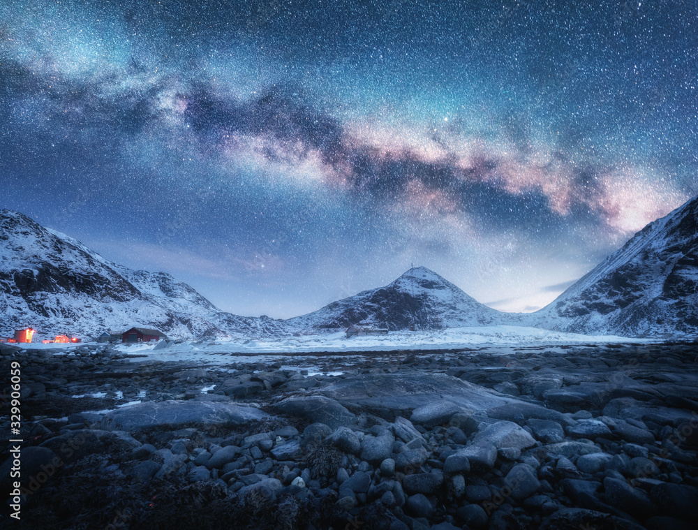 挪威罗弗敦群岛冬季夜晚白雪皑皑的山脉和石头海滩上的银河