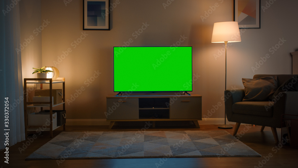 Shot of a TV with Horizontal Green Screen Mock Up. Cozy Evening Living Room with a Chair and Lamps T