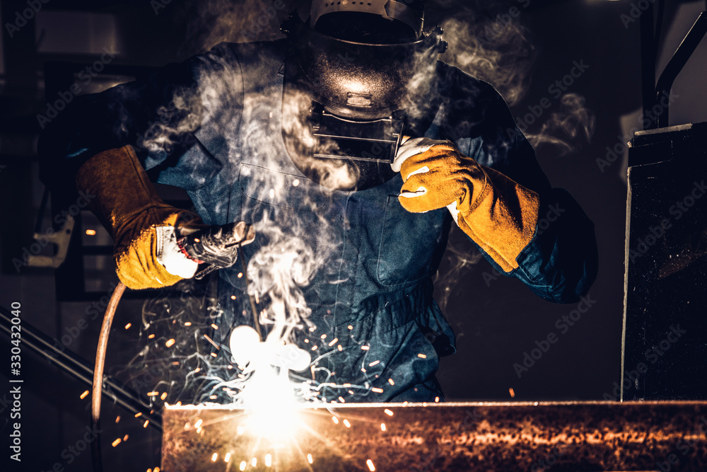 Metal welder working with arc welding machine to weld steel at factory while wearing safety equipmen