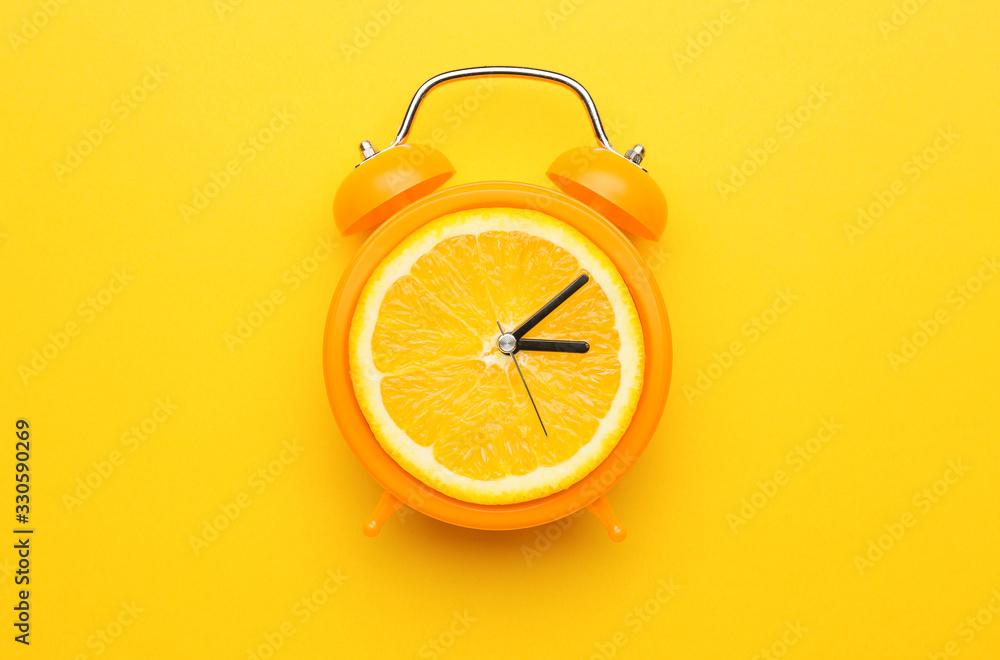 Creative alarm clock with citrus fruit on color background