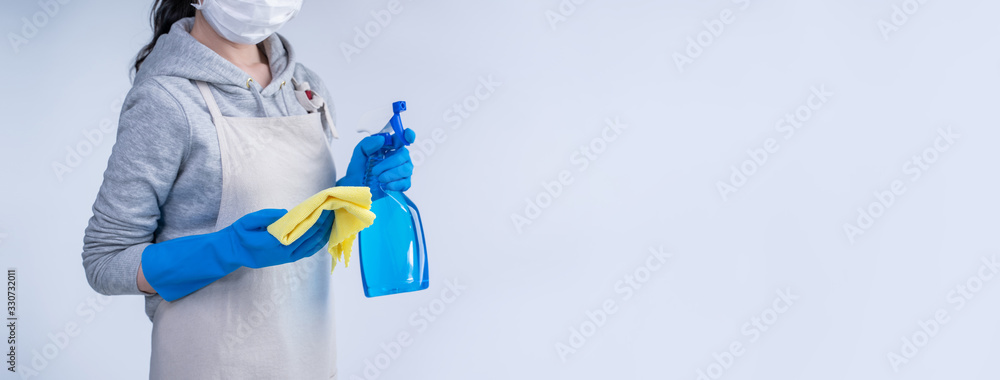 穿着围裙的年轻女管家正在用蓝色手套、湿黄色抹布、喷雾瓶进行清洁