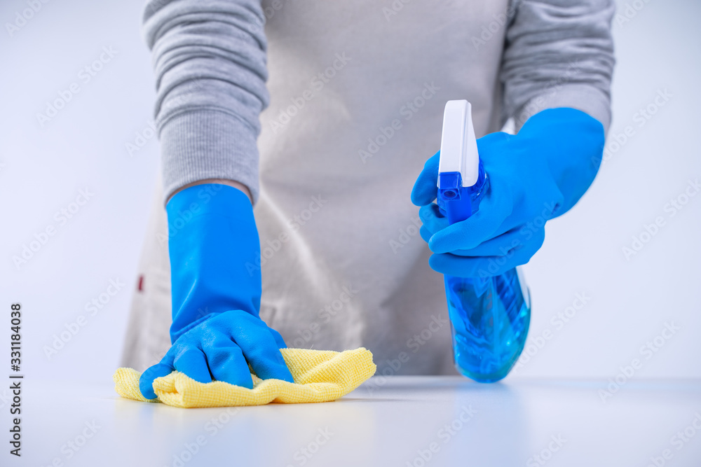 Young woman housekeeper in apron is cleaning, wiping down table surface with blue gloves, wet yellow