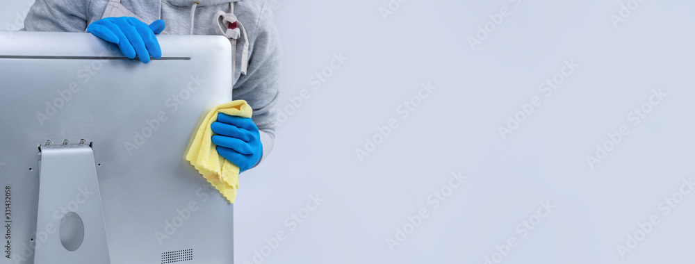 Young woman housekeeper in apron is cleaning silver computer surface with blue gloves, wet yellow ra