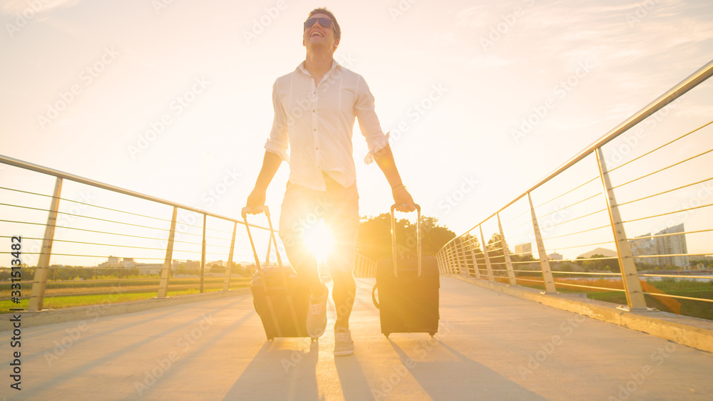 LENS FLARE: Funny shot of guy rushing to the airport with suitcases at sunset.