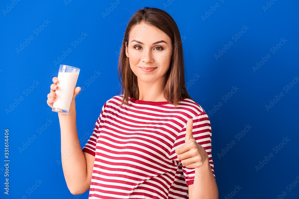 美丽的孕妇，一杯牛奶在彩色背景上竖起大拇指