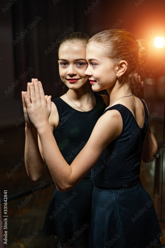 Portrait of attractive little ballerina touching mirror. Young ballet dancer at the mirror and her r