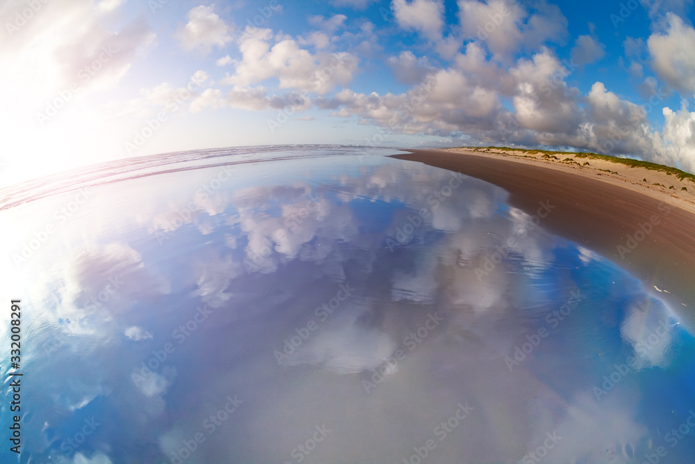 Cloudscape and reflection in the water of the ocean on California sand beach