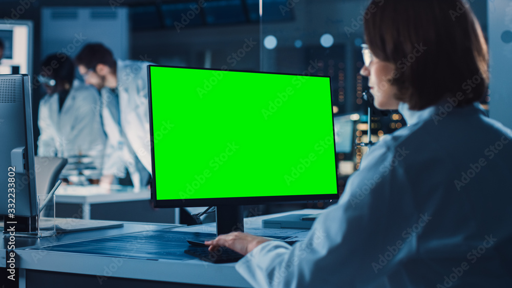肩上镜头：女IT科学家使用绿色实体屏幕电脑。背景技术