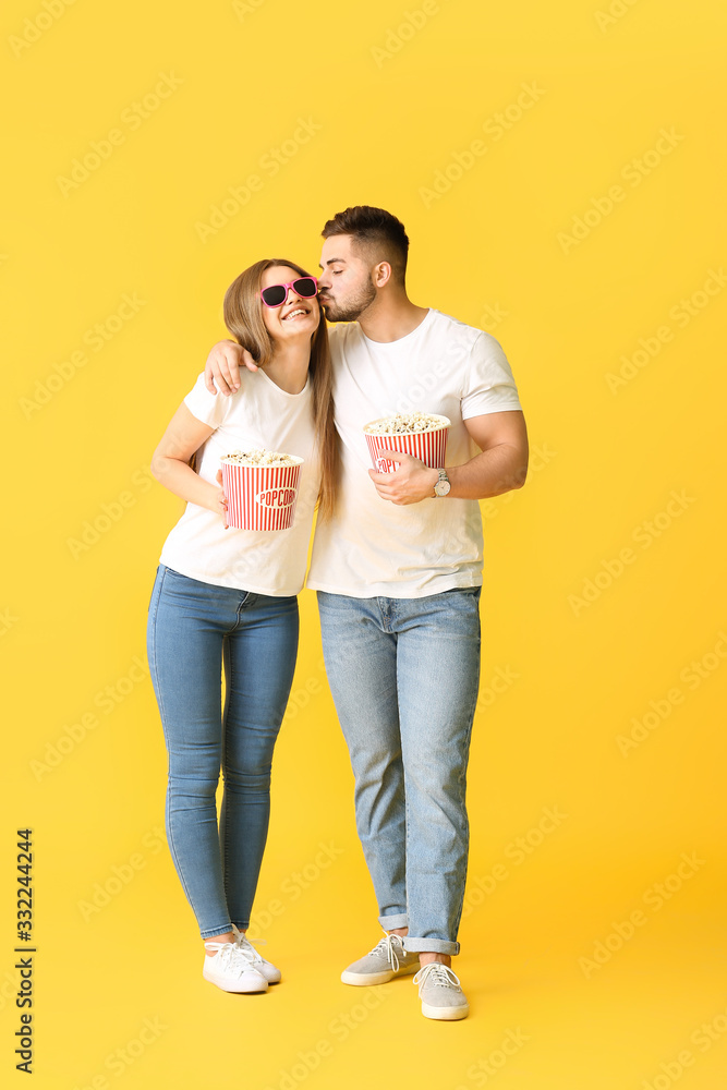 Happy young couple with popcorn watching movie on color background