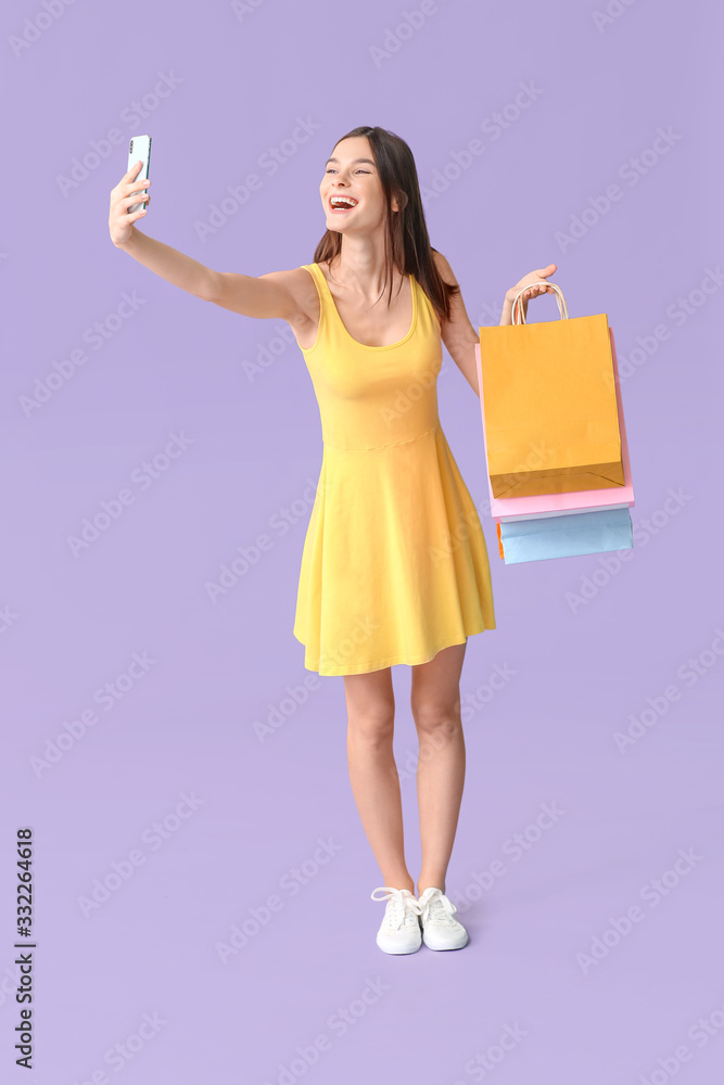 漂亮的年轻女人拿着购物袋在彩色背景下自拍