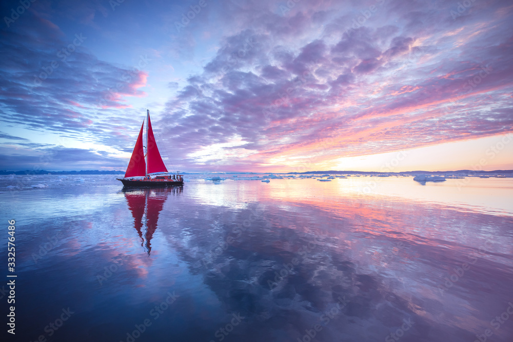 日出时，挂着红帆的帆船在冰山间巡航。格陵兰岛迪斯科湾。