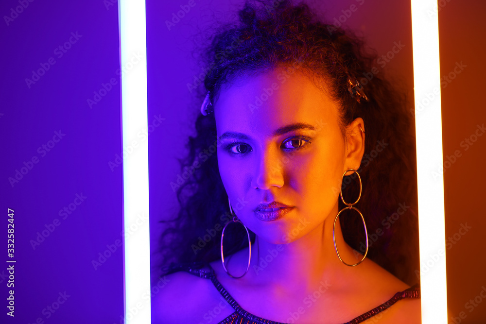 Beautiful African-American woman with neon lamps on color background