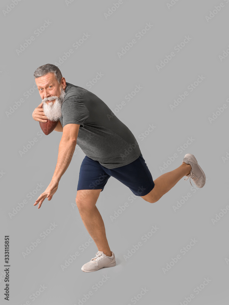 Sporty elderly man with rugby ball on grey background