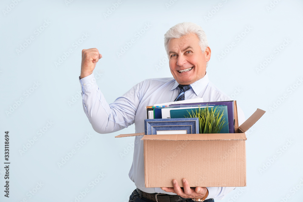 Happy fired mature man with personal stuff on color background