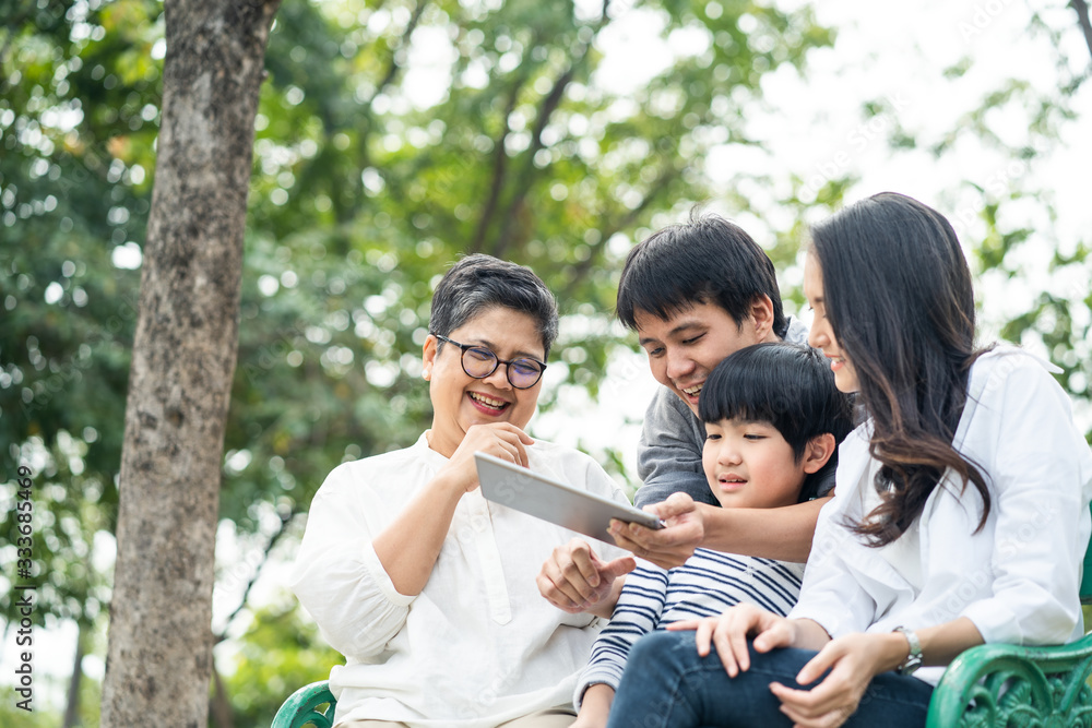 亚洲幸福家庭在公园玩耍，一起从平板电脑上读电子书。男孩坐在长椅上