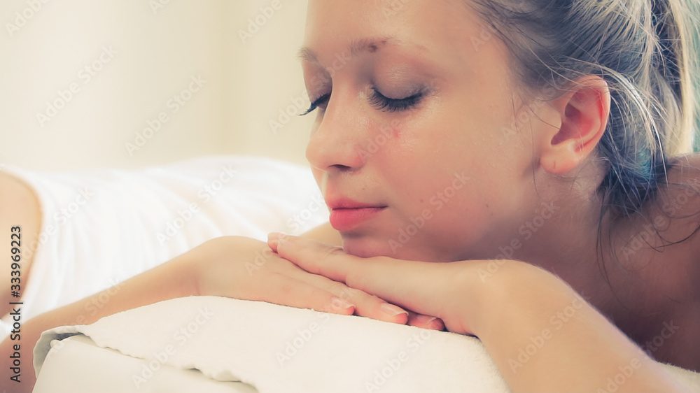 放松的年轻女子躺在水疗床上，准备在豪华水疗度假村进行面部护理和按摩。