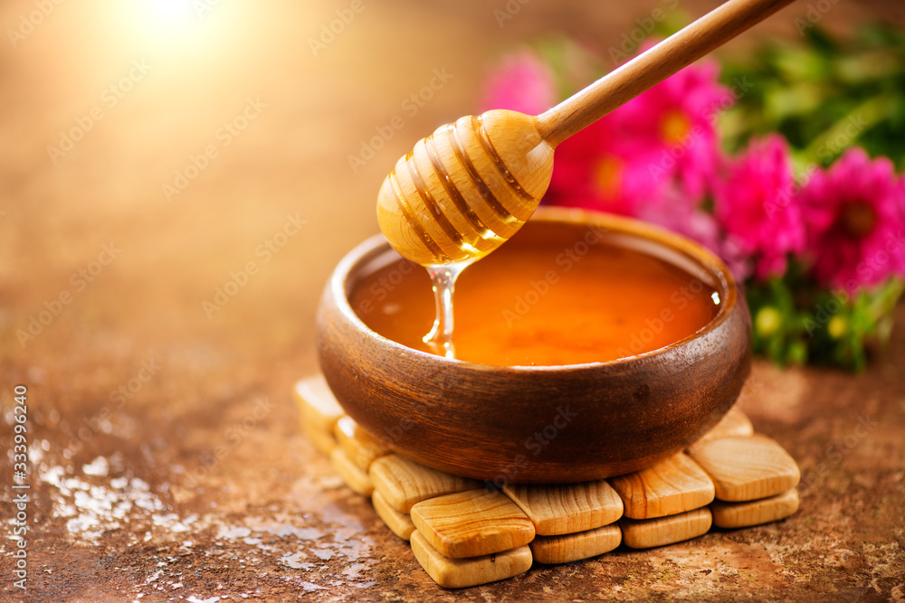 蜂蜜从木碗中的蜂蜜勺中滴下。特写。健康有机浓蜂蜜从中滴下