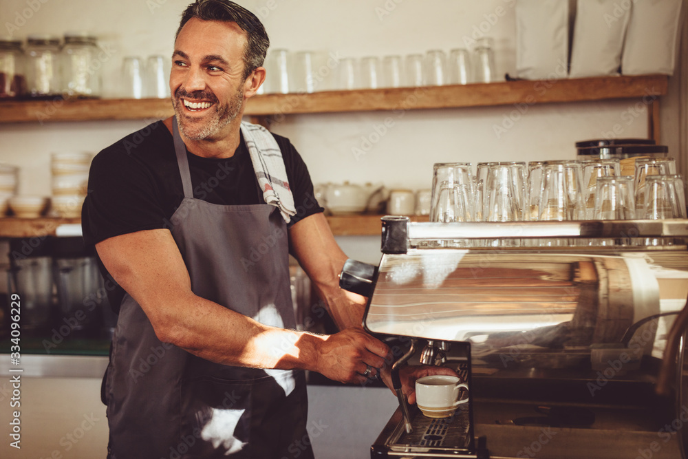 微笑的咖啡师用咖啡机制作浓缩咖啡