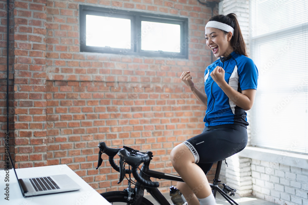 亚洲女自行车手。她在家里锻炼。在教练机上骑自行车，玩网上自行车