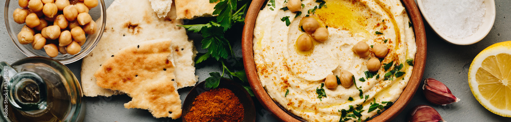 Large bowl of homemade hummus garnished with chickpeas, red sweet pepper, parsley and olive oil