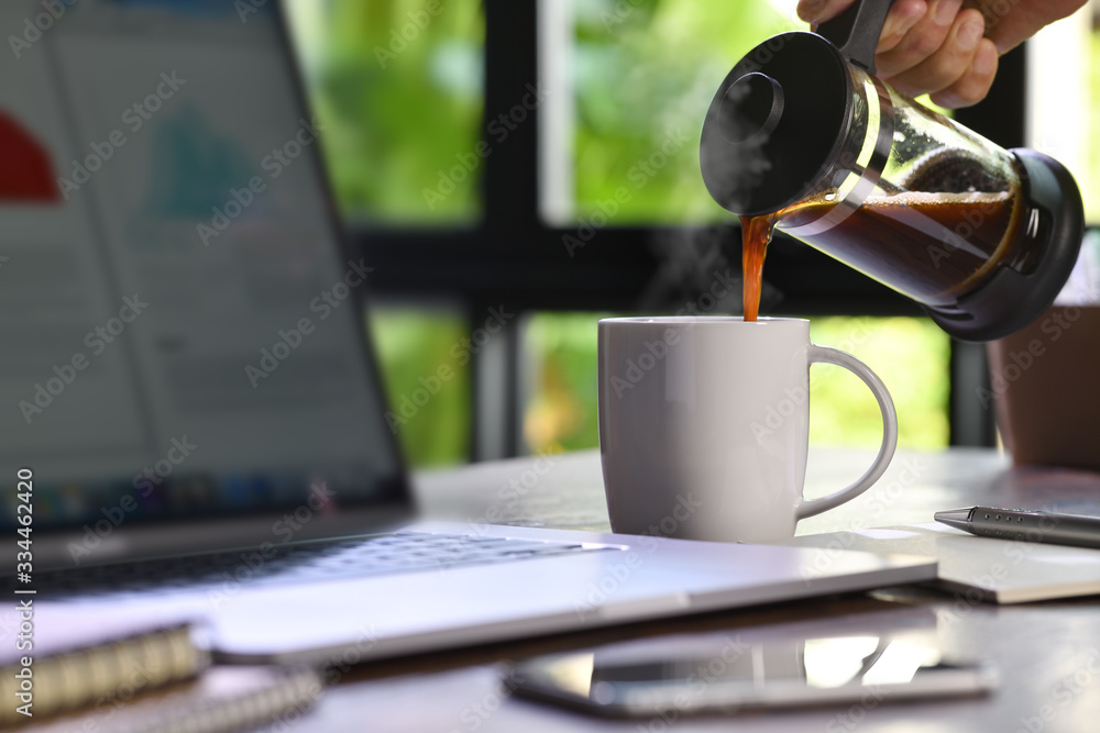 在家工作时，一只手把热气腾腾的咖啡倒进办公桌上的杯子里