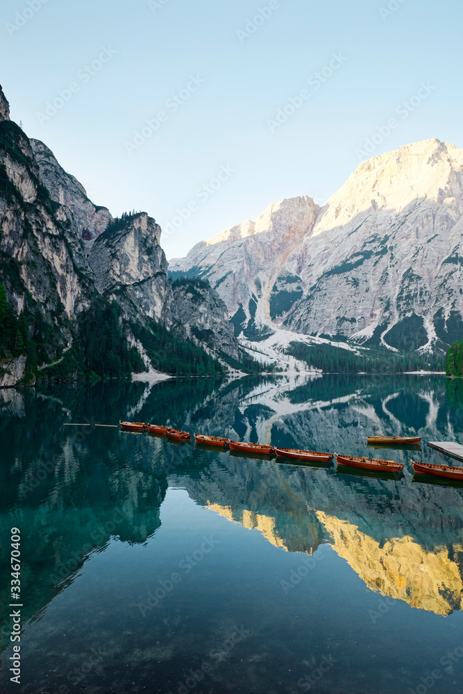 A row of wooden boats on Lake Braies, Dolomites, Italy. Reflection of mountains on clear lake under 