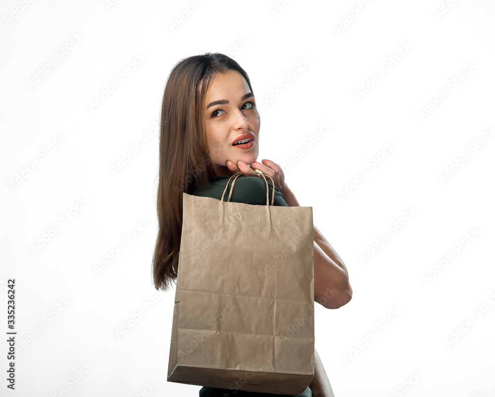 年轻女性拿着杂货购物袋。站在白色背景上。女性向后看。