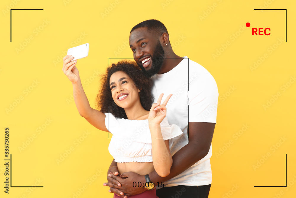 Portrait of happy African-American bloggers taking selfie on color background
