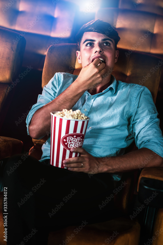 一个年轻人在电影院看电影时微笑着享用爆米花