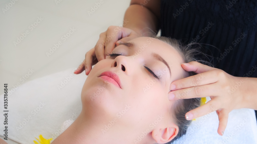 放松的女人躺在水疗床上，接受按摩师的面部和头部按摩水疗