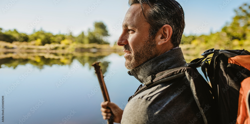 背着背包的成熟男人站在湖边。