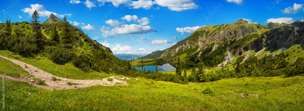 美丽的山脉环绕着一个湖泊，深蓝色的晴朗天空和前方的绿色草地