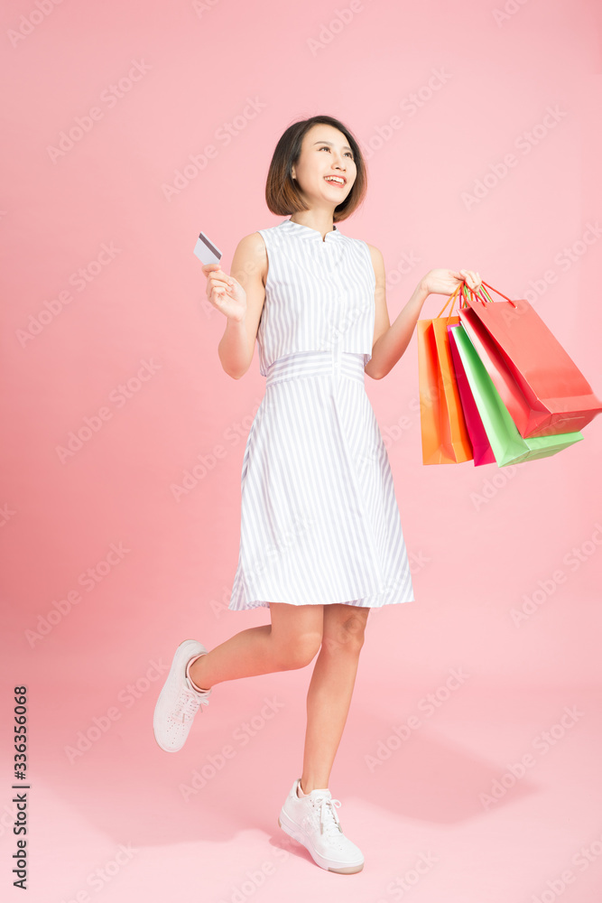 一个微笑的漂亮女孩的画像，她穿着连衣裙，拿着购物袋，手里拿着粉色隔离的信用卡