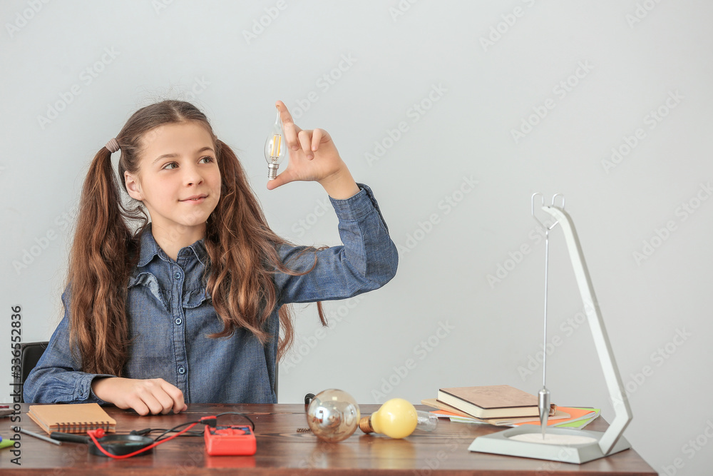 Cute little schoolgirl at table against grey background