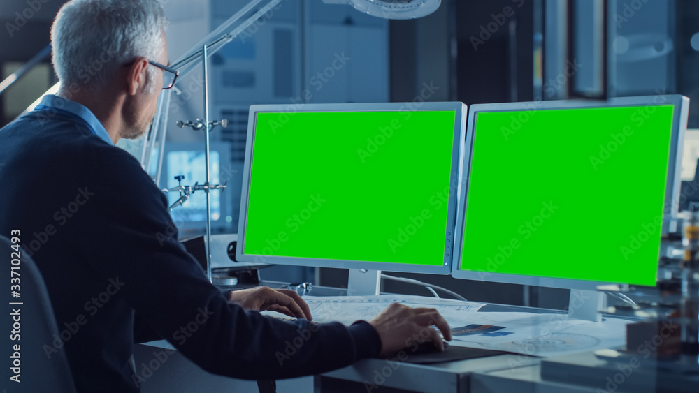 专业工程师在两个绿色实体屏幕显示器的计算机上工作。在后台