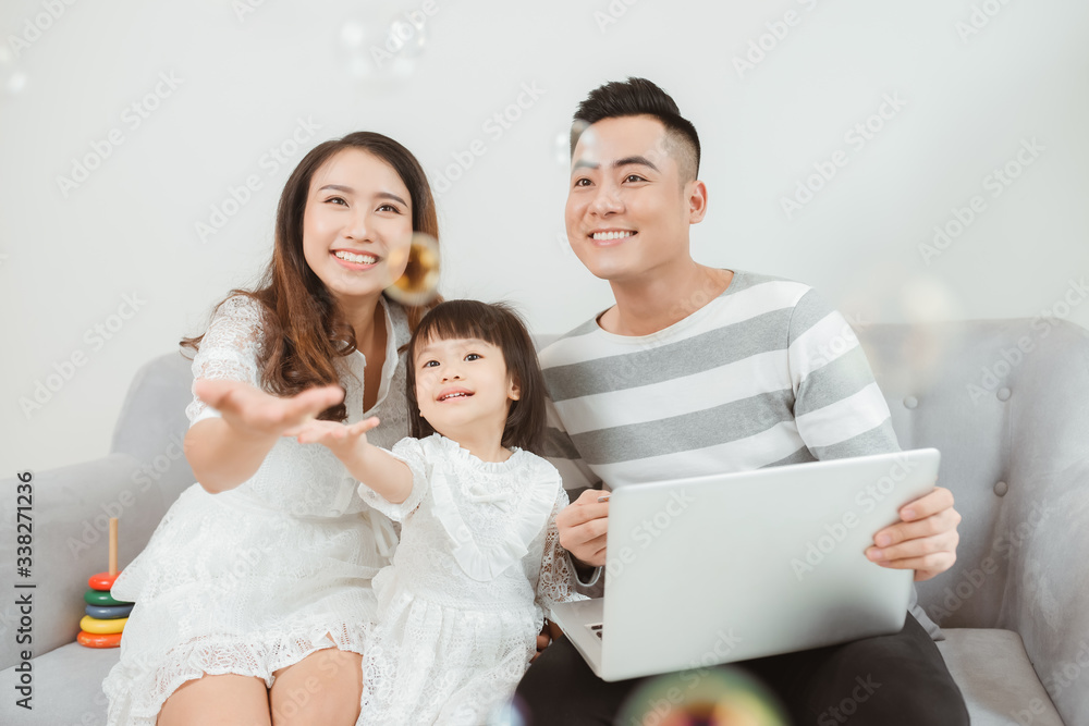 年轻家庭坐在家里的沙发上使用笔记本电脑。