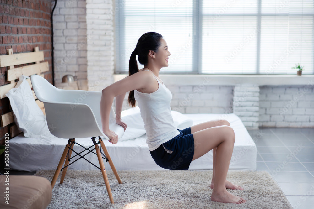 亚洲女性早上在家锻炼。她用椅子锻炼。增加手臂肌肉