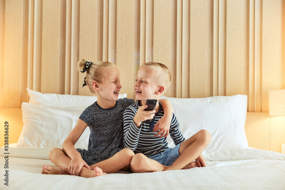Laughing little girl hugging her brother while watching tv toget