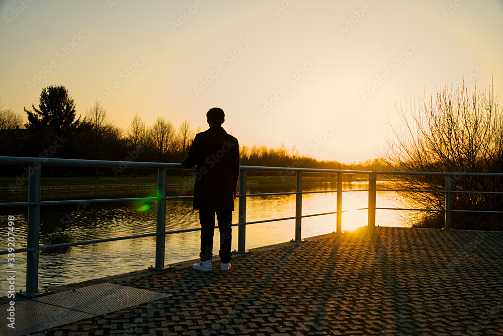 Silhouette of young man watching the sunset before fence by lake, copy space