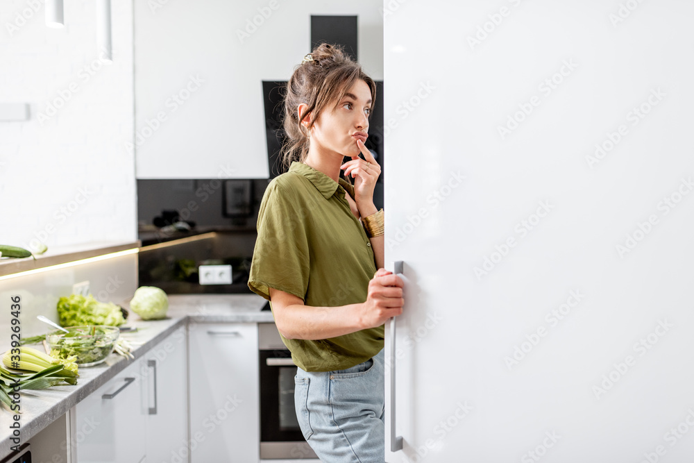 女人在家里的现代厨房里烹饪健康食品时看着冰箱