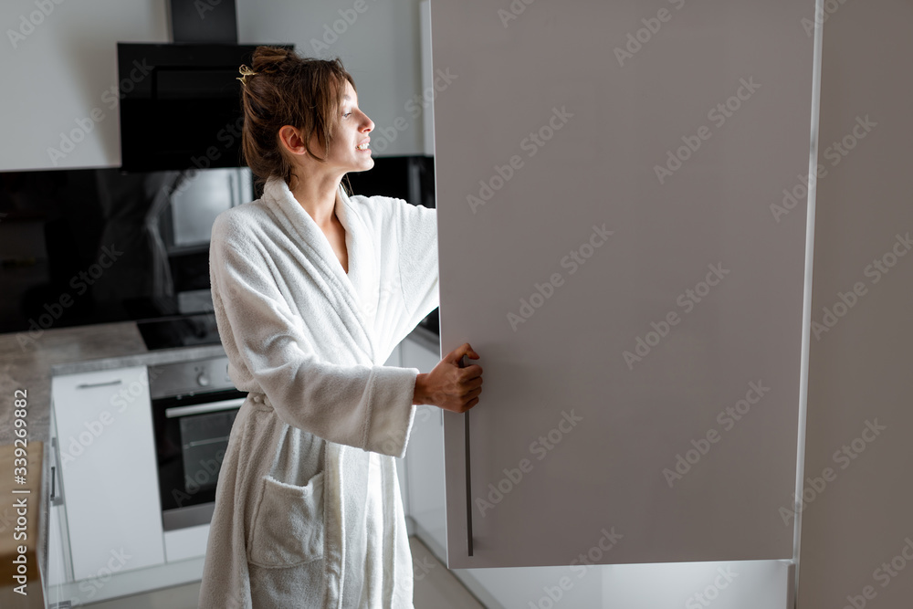 Young woman in bathrobe getting some food from the fridge, feeling hungry at night. Concept of not r