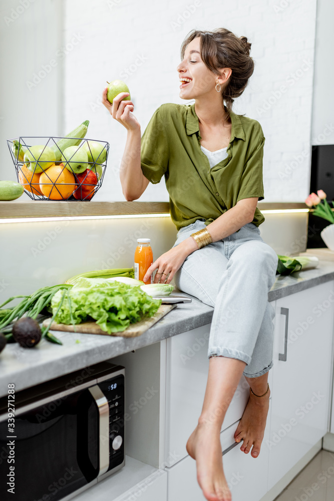 一位年轻开朗的女性在家里的厨房里吃着健康的生食的全长肖像。素食主义者