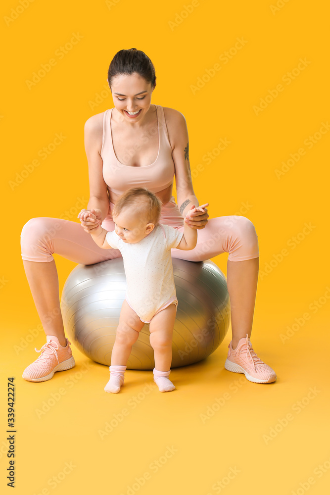 年轻的运动型妈妈和她的宝宝在彩色背景下用健身球做运动