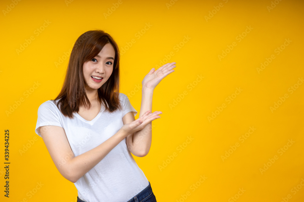 年轻优雅的亚洲女性微笑着，指着黄色背景上隔离的空复制空间